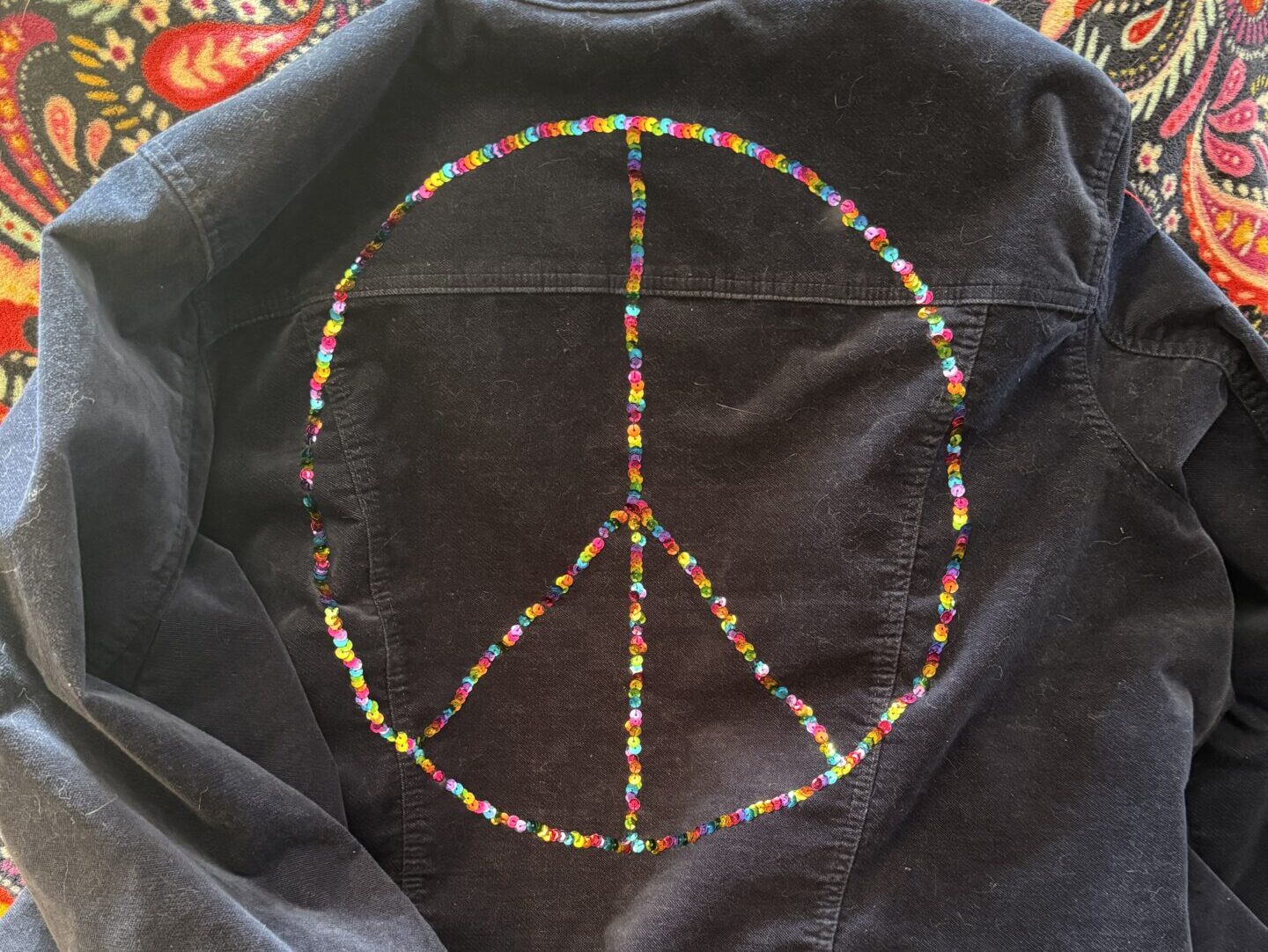 Blue jacket wth rainbow sequins in the shape of a peace sign on the back.