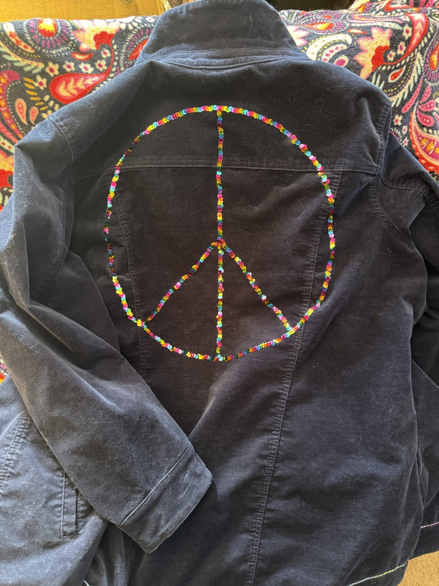 Blue jacket wth rainbow sequins in the shape of a peace sign on the back.